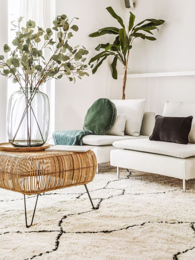 Bright, airy living room with white sofa, rattan table, eucalyptus vase, and a geometric rug.