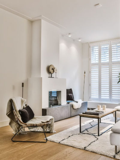 Modern, light-filled living room featuring a fireplace, cozy seating, wood floor, and white shutters.